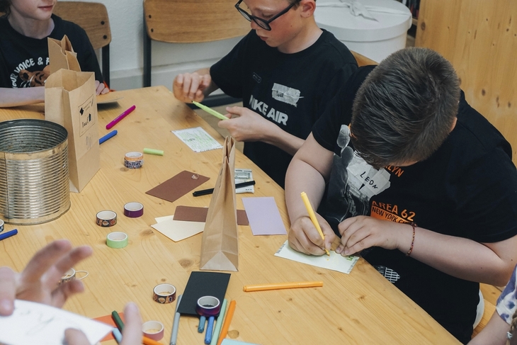 Kinder basteln an einem Tisch mit Papier und Stiften.