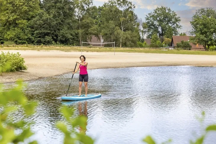 Person auf einem SUP-Board auf einem Badesee vor Sandstrand und Bäumen am Eurostrand Resort.