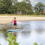 Person auf einem SUP-Board auf einem Badesee vor Sandstrand und Bäumen am Eurostrand Resort.