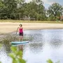 Person auf einem SUP-Board auf einem Badesee vor Sandstrand und Bäumen am Eurostrand Resort.