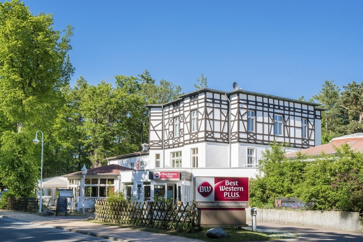 Fachwerkgebäude des Best Western Plus Ostseehotels Waldschlösschen in Prerow, umgeben von Bäumen.