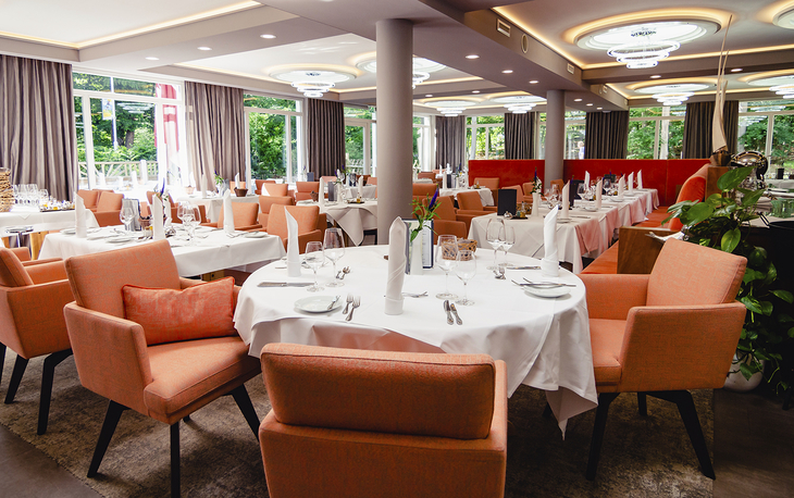 Restaurant mit gedeckten Tischen und orangen Stühlen im Ostseehotel Waldschlösschen.