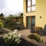 Rückansicht eines Hauses mit Terrasse, Pflanzen und Gartenmöbeln.