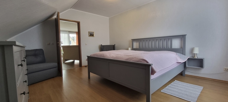 Schlafzimmer mit grauem Bett, Sessel und Holzfußboden.