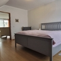 Schlafzimmer mit grauem Bett, Sessel und Holzfußboden.