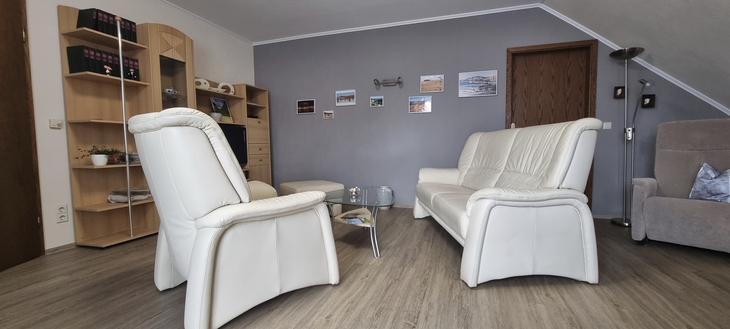 Wohnzimmer mit weißen Ledersofas und Regal an grauer Wand.