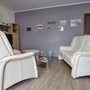 Wohnzimmer mit weißen Ledersofas und Regal an grauer Wand.