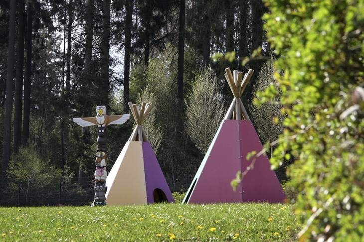Zwei bunte Tipis und ein Totempfahl auf einer Wiese im Wald der Ferienanlage Prüm.
