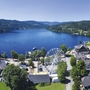 Luftaufnahme eines Sees mit Riesenrad und umliegender Stadt in einer grünen Landschaft.