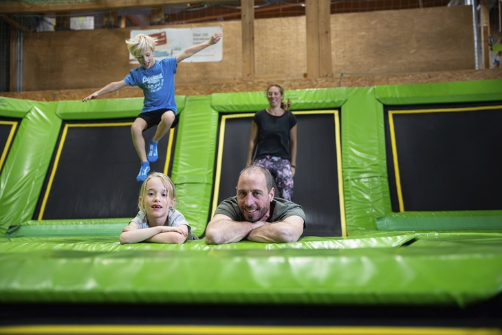 Familie springt auf Trampolinen in einer Indoor-Freizeithalle.