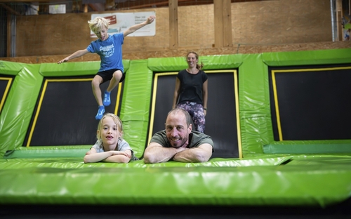 Familie springt auf Trampolinen in einer Indoor-Freizeithalle.