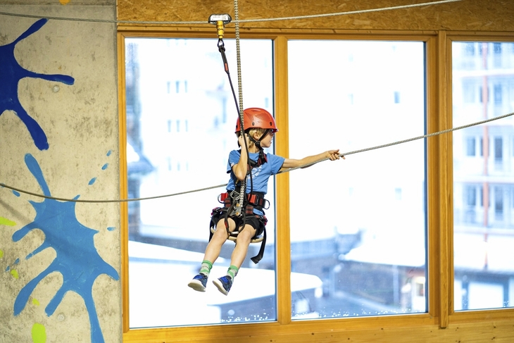Kind mit Helm auf Seilrutsche in Indoor-Freizeitzentrum.