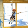 Kind mit Helm auf Seilrutsche in Indoor-Freizeitzentrum.
