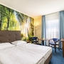 Helles Hotelzimmer mit Doppelbett, Waldtapete und blauen Vorhängen.