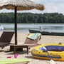 Strand mit Liegen, Sonnenschirm und gelbem aufblasbarem Paddelboot am Seeufer.