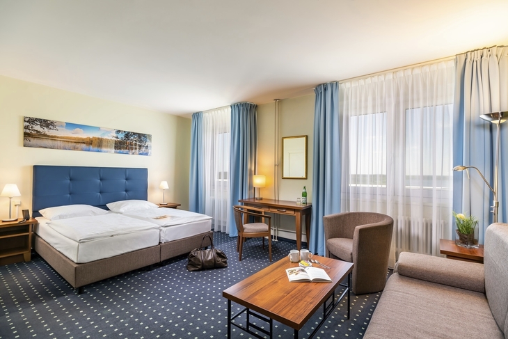 Helles Hotelzimmer mit Doppelbett, Schreibtisch und Seeblick in Templin.