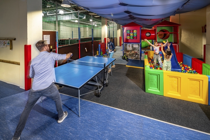 Kinder spielen in einer bunten Indoor-Spielwelt mit Ballpool und Tischtennisplatte.