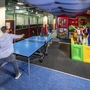 Kinder spielen in einer bunten Indoor-Spielwelt mit Ballpool und Tischtennisplatte.