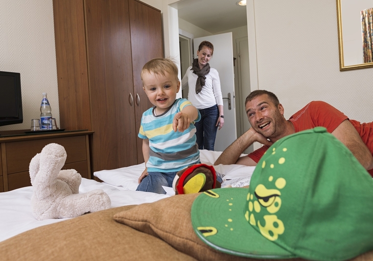Mann, Kind und Frau spielen lächelnd in einem Familienzimmer.