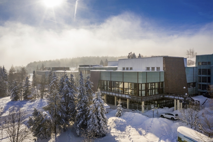 Winterliches Waldhotel Altenberg im Schnee, umgeben von verschneiten Bäumen und sonnigem Himmel.