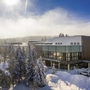 Winterliches Waldhotel Altenberg im Schnee, umgeben von verschneiten Bäumen und sonnigem Himmel.