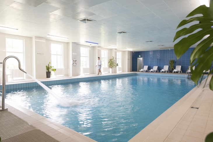 Innenpool im Ahorn Waldhotel Altenberg mit Liegestühlen und Pflanzen.