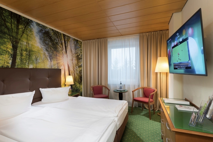 Hotelzimmer mit Doppelbett, Waldtapete, Fernseher, Fenster und Sitzbereich.