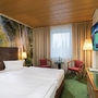 Hotelzimmer mit Doppelbett, Waldtapete, Fernseher, Fenster und Sitzbereich.