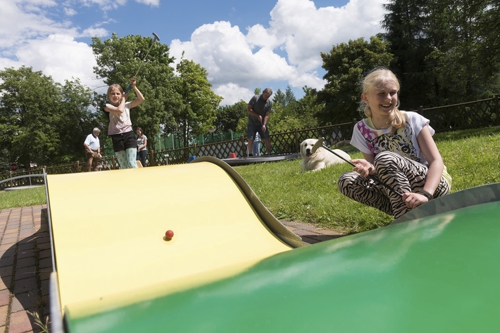 Kinder spielen Minigolf im Freien bei sonnigem Wetter.