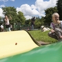 Kinder spielen Minigolf im Freien bei sonnigem Wetter.