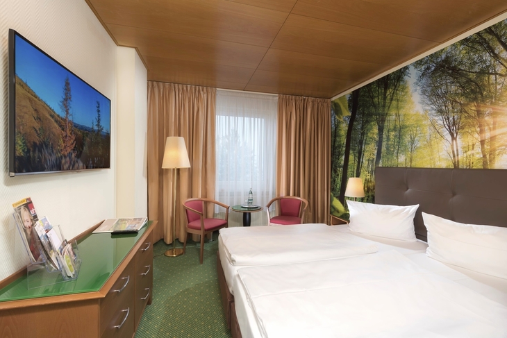 Hotelzimmer mit Doppelbett, Waldmotiv an der Wand und Flachbild-TV.