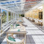 Heller Wintergarten eines Hotels mit gedeckten Tischen und Blick ins Grüne.