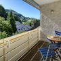 Balkon mit Tisch und Stühlen, Blick auf Hügel und Bäume im Hintergrund.