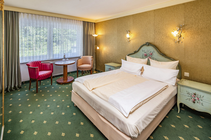 Hotelzimmer mit Doppelbett, zwei Sesseln und einem Tisch, floral dekoriert.