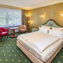 Hotelzimmer mit Doppelbett, zwei Sesseln und einem Tisch, floral dekoriert.