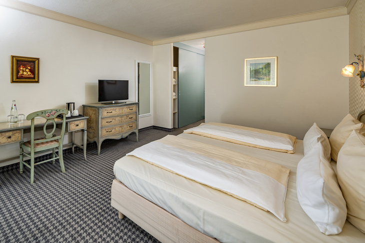 Doppelzimmer im Hotel mit zwei Betten, TV, Schreibtisch und dekorativer Wandkunst.