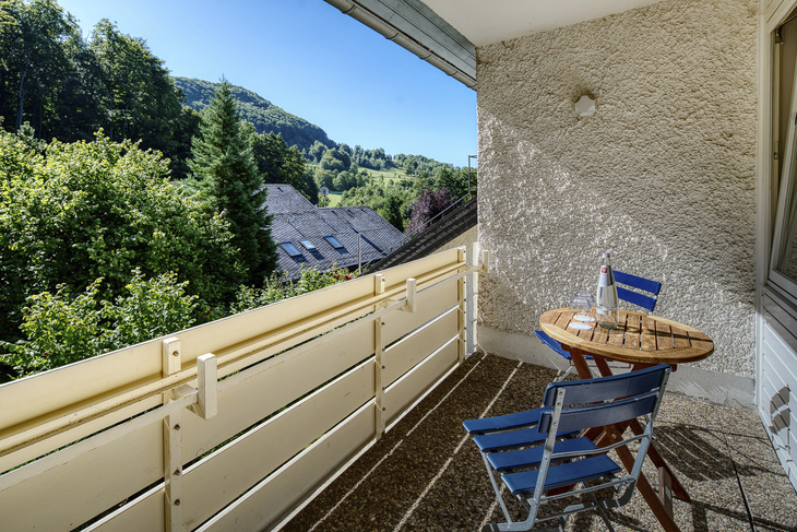 Balkon mit Tisch und Stühlen, Blick auf Hügel und Bäume im Hintergrund.