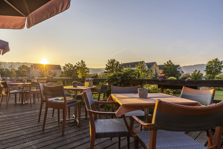 Außenterrasse mit Tischen und Stühlen bei Sonnenuntergang im Eurostrand Resort Moseltal.