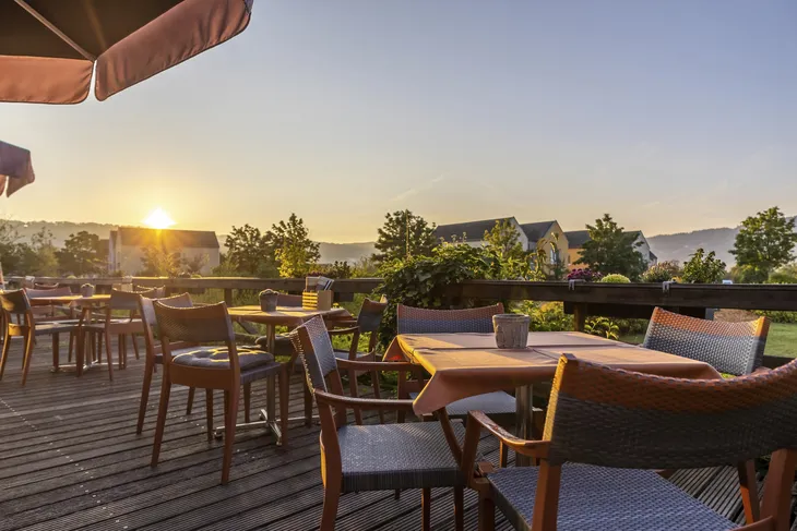 Außenterrasse mit Tischen und Stühlen bei Sonnenuntergang im Eurostrand Resort Moseltal.