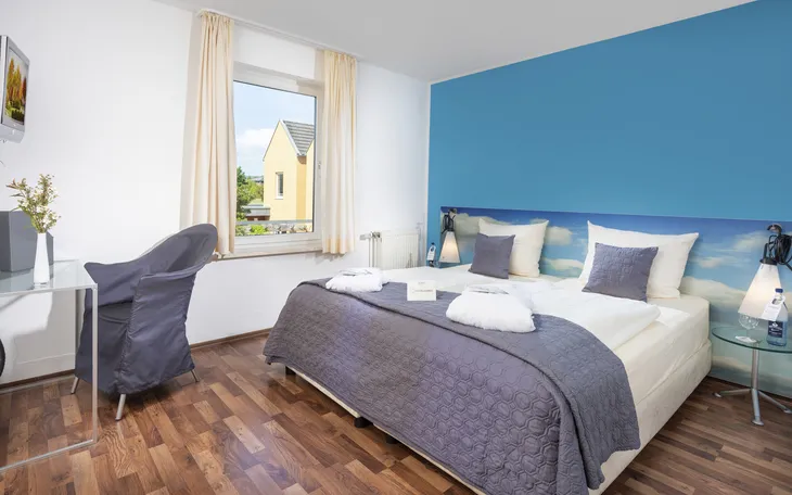 Modernes Schlafzimmer mit blauem Akzent, Doppelbett und Tageslicht im Eurostrand Resort Moseltal.