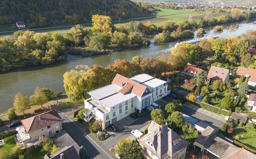 Drohnenaufnahme des Karlstadt Hotels an der Mainpromenade in herbstlicher Landschaft.