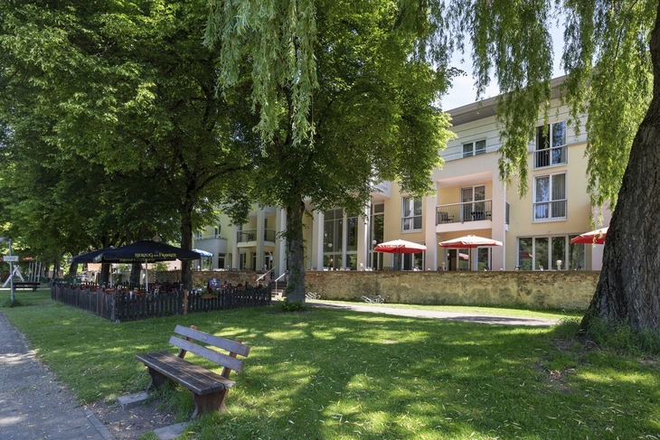 Hotel mit Biergarten und Bäumen außen bei Sonnenschein.