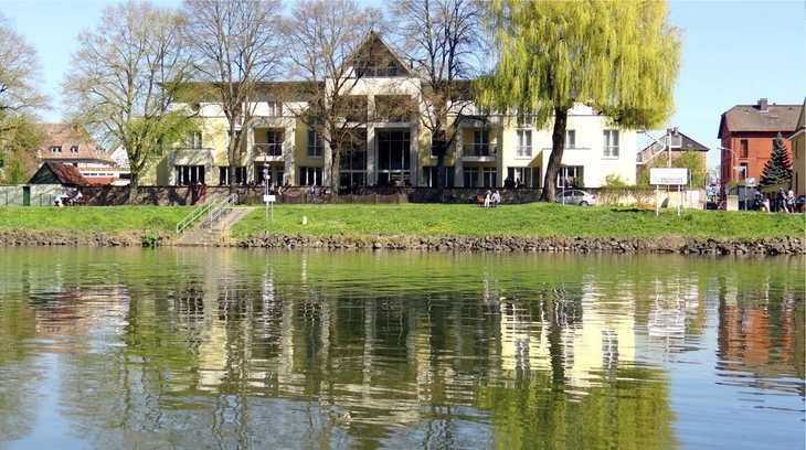 Außenansicht eines Hotels an einer Promenade mit Spiegelung im Wasser.