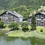 Appartementanlage am See mit bewaldeten Hügeln im Hintergrund