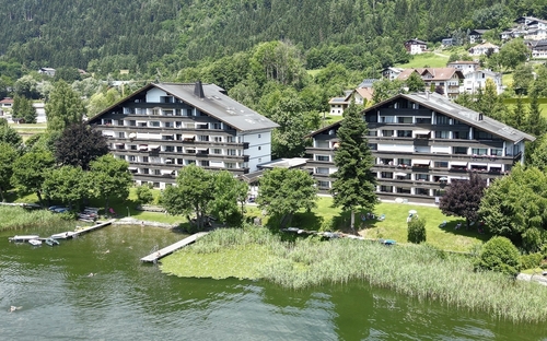 Appartementanlage am See mit bewaldeten Hügeln im Hintergrund