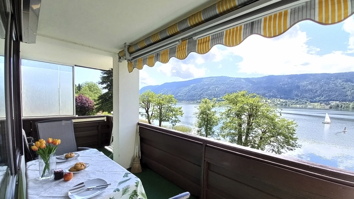 Balkon mit Tisch und Aussicht auf See und Berge bei sonnigem Wetter