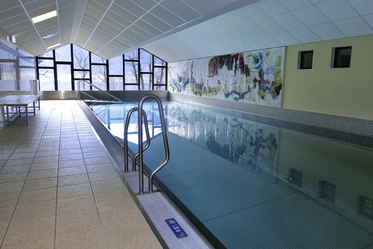Innenansicht eines Schwimmbads mit Wandmalerei und großen Fenstern.