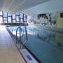 Innenansicht eines Schwimmbads mit Wandmalerei und großen Fenstern.