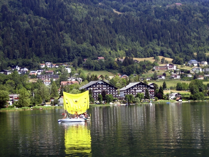 Appartementanlage am See mit Wald im Hintergrund.