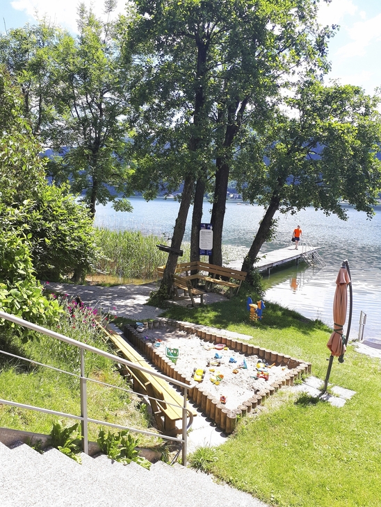 Garten mit Sandkasten und Blick auf einen See im Hintergrund.